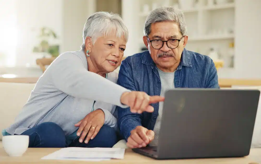 An older couple reviewing something on a laptop together, pointing at the screen, suggesting they’re addressing taxes, checking filings, or getting clarity on their financial situation.